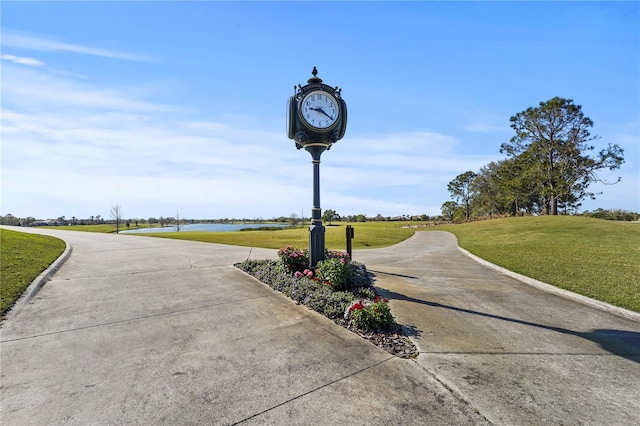 surrounding community with a lawn, concrete driveway, and a water view