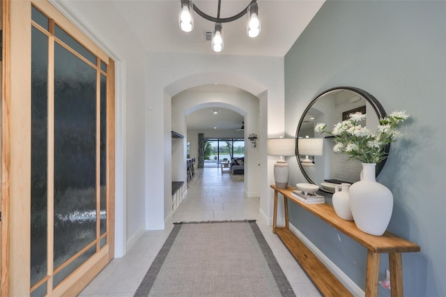 hall featuring arched walkways, visible vents, baseboards, and an inviting chandelier
