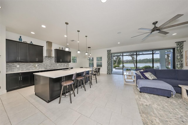 kitchen with open floor plan, light countertops, a water view, a sink, and wall chimney range hood