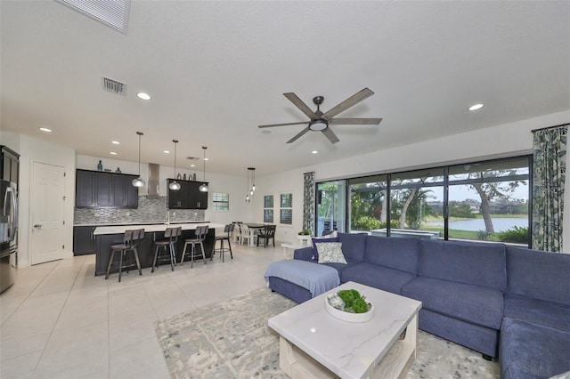living room with a ceiling fan, light tile patterned floors, visible vents, a water view, and recessed lighting