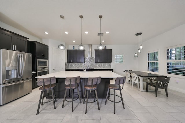 kitchen featuring light countertops, backsplash, a kitchen bar, stainless steel appliances, and wall chimney range hood