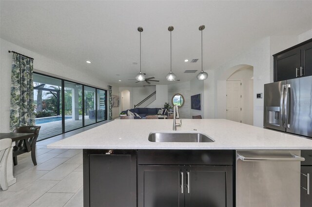kitchen featuring a kitchen island with sink, a ceiling fan, arched walkways, a sink, and open floor plan