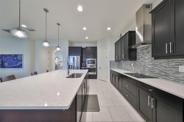 kitchen featuring a sink, appliances with stainless steel finishes, wall chimney range hood, visible vents, and decorative backsplash