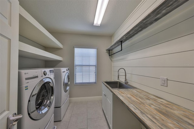 washroom with a textured ceiling, a sink, washer and dryer, cabinet space, and light tile patterned floors