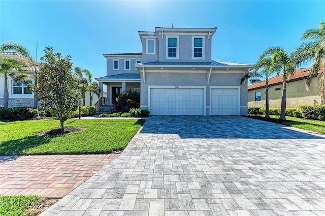 view of front of house with metal roof, decorative driveway, stucco siding, a front lawn, and a standing seam roof