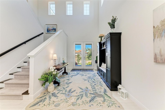 entryway with a healthy amount of sunlight, stairs, a towering ceiling, and french doors