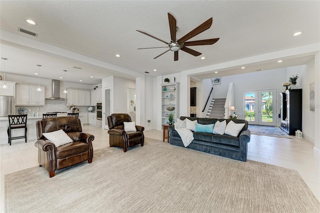 living area with a textured ceiling, recessed lighting, visible vents, stairs, and french doors