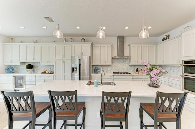 kitchen with wine cooler, stainless steel appliances, visible vents, a sink, and wall chimney exhaust hood