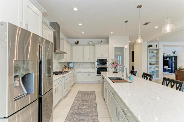 kitchen featuring tasteful backsplash, visible vents, appliances with stainless steel finishes, a sink, and wall chimney range hood