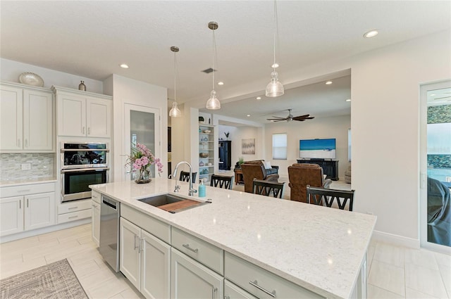 kitchen featuring tasteful backsplash, hanging light fixtures, a kitchen island with sink, stainless steel appliances, and a sink