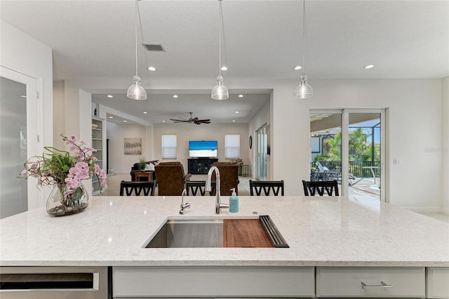 kitchen with recessed lighting, hanging light fixtures, open floor plan, a sink, and light stone countertops