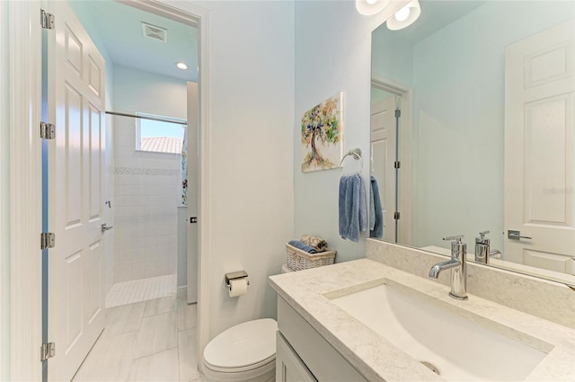 bathroom featuring visible vents, a tile shower, vanity, and toilet