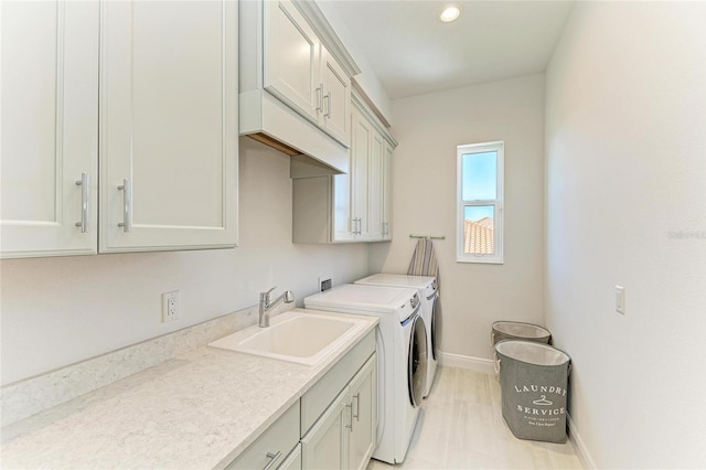 clothes washing area with cabinet space, washing machine and dryer, baseboards, and a sink