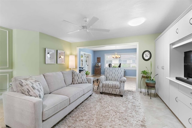 living area with light tile patterned flooring, baseboards, and ceiling fan with notable chandelier