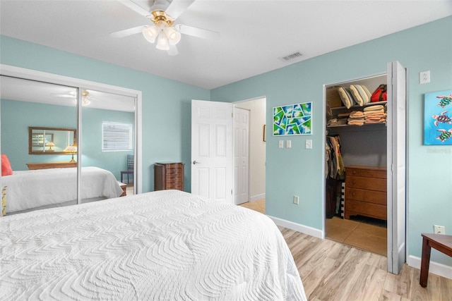 bedroom with a walk in closet, a closet, visible vents, light wood-style flooring, and a ceiling fan