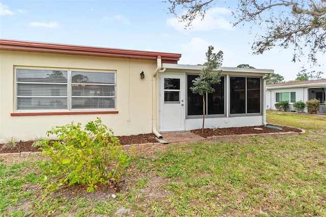 rear view of house featuring a lawn, a sunroom, and stucco siding