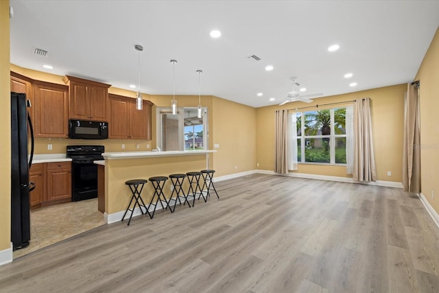 kitchen with light wood finished floors, black appliances, a breakfast bar, and visible vents