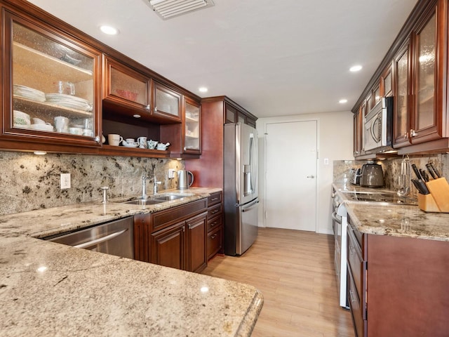 kitchen with stainless steel appliances, visible vents, light wood-style flooring, a sink, and light stone countertops