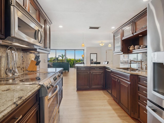 kitchen featuring visible vents, a peninsula, stainless steel appliances, light wood-style floors, and a sink