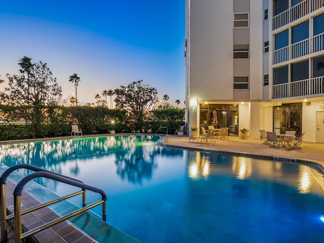 pool at dusk featuring a patio and a community pool