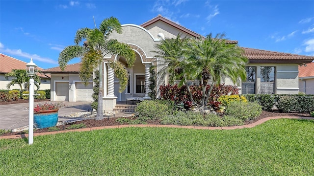 mediterranean / spanish home featuring a garage, driveway, a front yard, and stucco siding