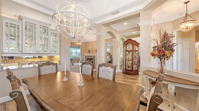 dining space with ornate columns, an inviting chandelier, crown molding, light wood-style floors, and a fireplace