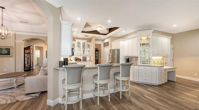 6621 The Masters Ave, Lakewood Ranch, FL 34202 - kitchen with arched walkways, freestanding refrigerator, a peninsula, wood finished floors, and glass insert cabinets