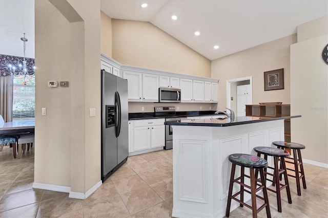 kitchen featuring white cabinets, dark countertops, appliances with stainless steel finishes, a kitchen bar, and high vaulted ceiling