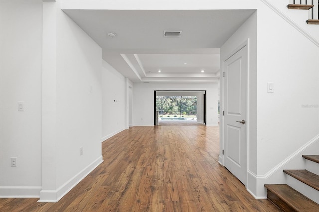 corridor with a tray ceiling, wood finished floors, baseboards, and stairs