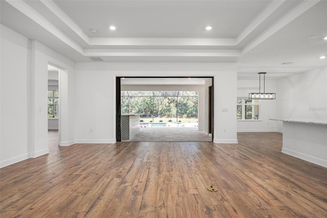 unfurnished living room featuring a wealth of natural light, a raised ceiling, baseboards, and wood finished floors