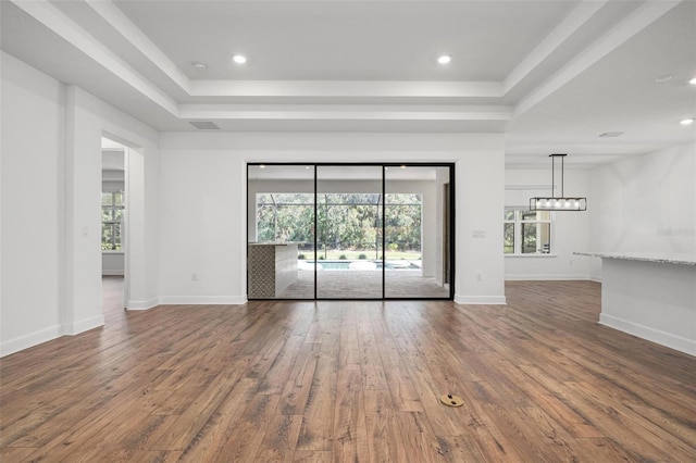 unfurnished living room with a tray ceiling, a healthy amount of sunlight, and wood finished floors