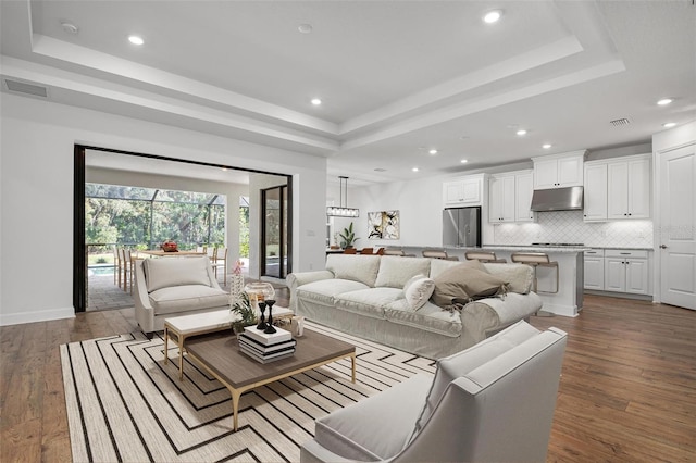 living room with a tray ceiling, wood-type flooring, and visible vents