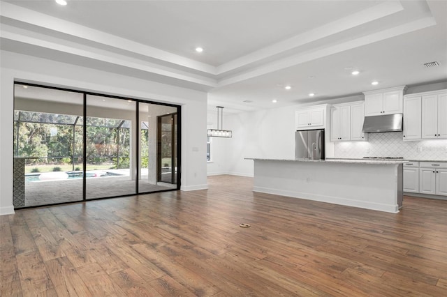 unfurnished living room featuring dark wood-style floors, a tray ceiling, recessed lighting, visible vents, and baseboards