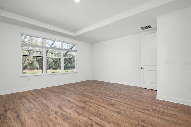 spare room featuring a tray ceiling, visible vents, baseboards, and wood finished floors