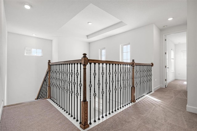 corridor with baseboards, a raised ceiling, carpet flooring, an upstairs landing, and recessed lighting