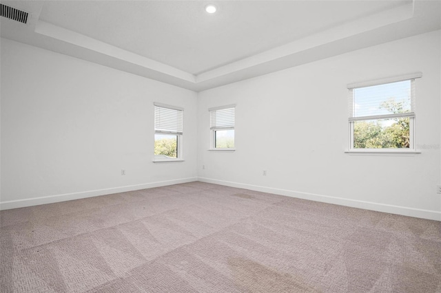 unfurnished room featuring a raised ceiling, light carpet, visible vents, and baseboards