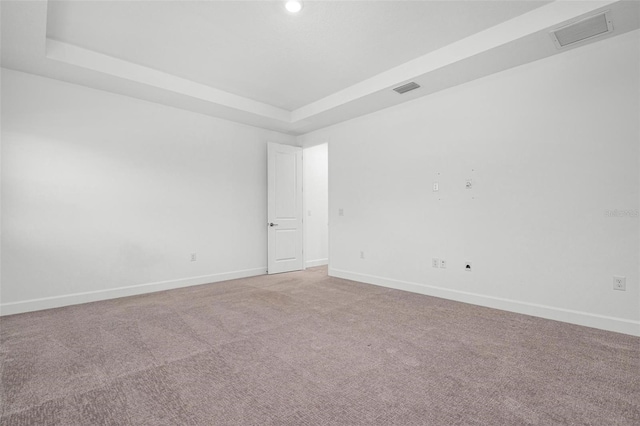 unfurnished room with a tray ceiling, visible vents, light carpet, and baseboards