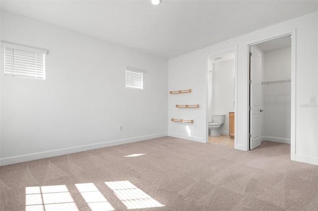 unfurnished bedroom featuring a closet, a spacious closet, ensuite bathroom, carpet flooring, and baseboards