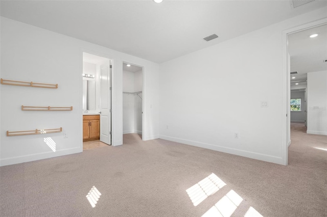 unfurnished bedroom featuring light carpet, baseboards, visible vents, and a walk in closet