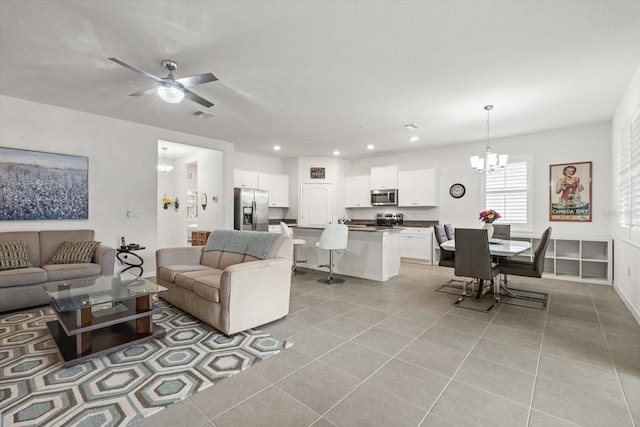 living room with light tile patterned floors, recessed lighting, visible vents, baseboards, and ceiling fan with notable chandelier