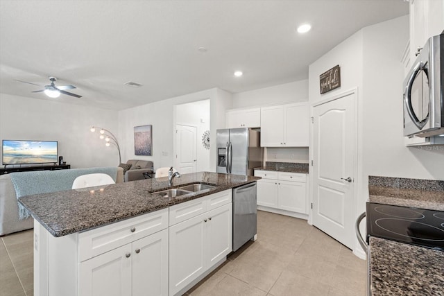 kitchen featuring open floor plan, stainless steel appliances, dark stone counters, and a sink