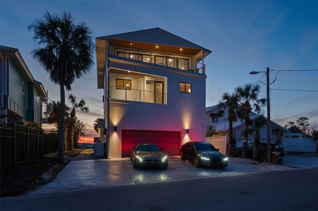 view of front of house with an attached garage, a balcony, fence, driveway, and stucco siding