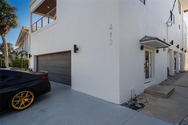 view of side of home featuring an attached garage, a balcony, and stucco siding