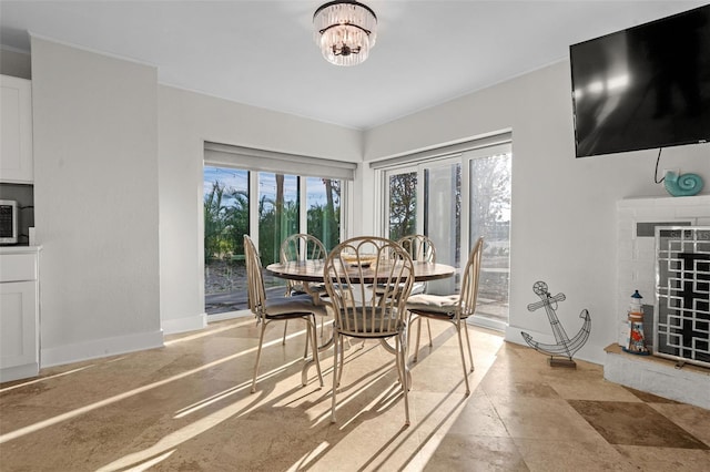 dining space featuring a healthy amount of sunlight, an inviting chandelier, a fireplace, and baseboards