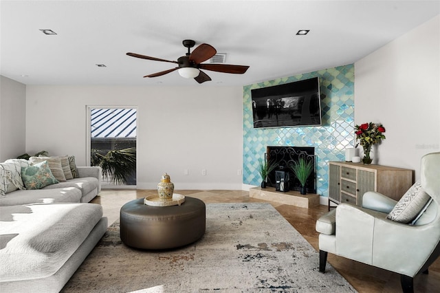 living area with an accent wall, a fireplace, a ceiling fan, and baseboards