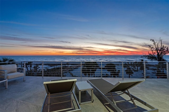 patio terrace at dusk featuring a water view and a balcony