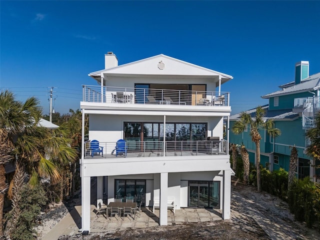 rear view of house featuring a patio, a balcony, an outdoor hangout area, stucco siding, and a chimney