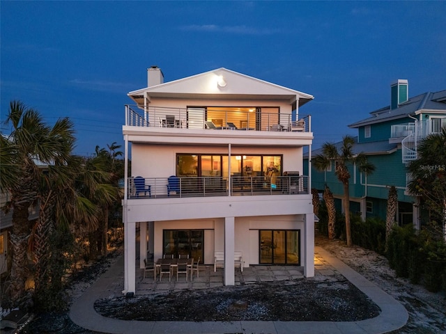 back of house featuring a chimney, a patio area, a balcony, and stucco siding