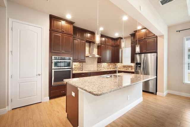 kitchen with visible vents, a sink, stainless steel appliances, wall chimney exhaust hood, and backsplash