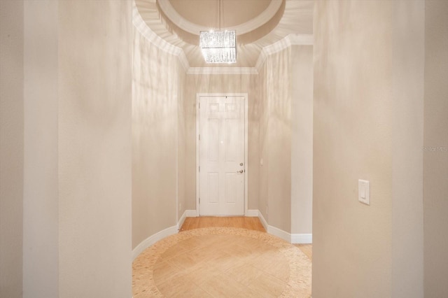 hall with a chandelier, wood finished floors, baseboards, and ornamental molding